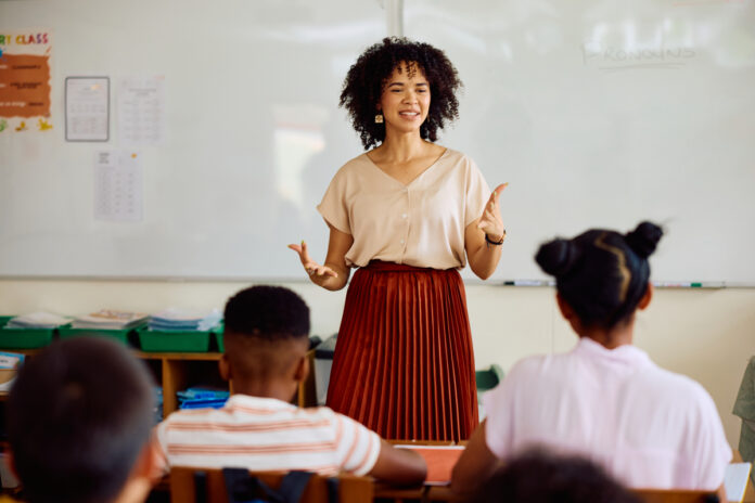 Elementary school teacher at front of class talking to children, gesturing Novo professor é mentor, mediador e criador de futuros
